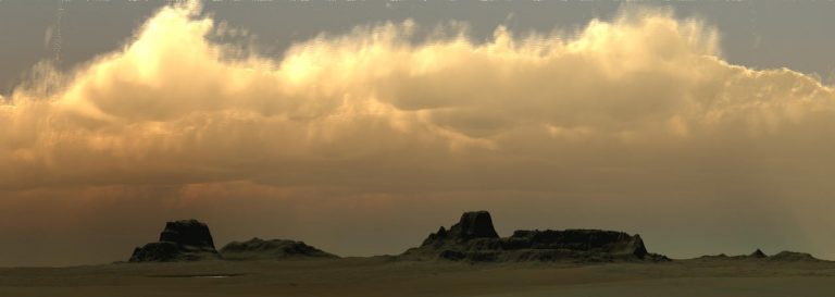 A panoramic view of a desert landscape with rocky formations under a cloudy sky during sunset.